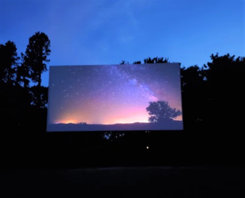 A large screen displays a starry night sky with a colorful horizon, surrounded by dark silhouettes of trees.
