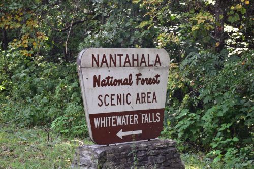 Sign for Nantahala National Forest Scenic Area, directing to Whitewater Falls, surrounded by greenery.