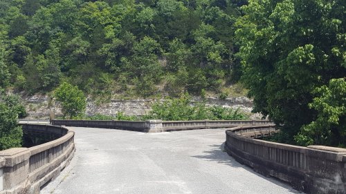 A winding road splits into two paths, surrounded by lush greenery and rocky cliffs.