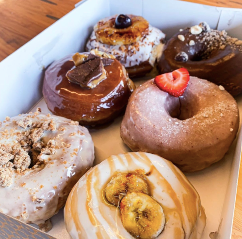 A box of six assorted donuts, featuring various toppings like chocolate, fruit, and caramel.