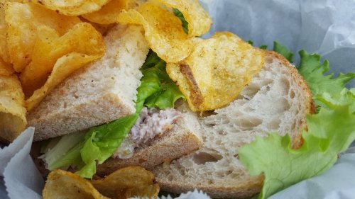 A close-up of a sandwich with lettuce and a side of crispy potato chips in a paper-lined basket.
