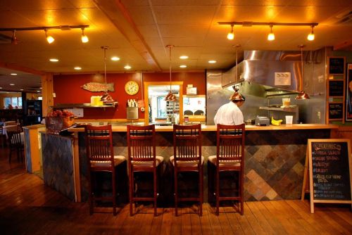 A cozy restaurant interior with wooden chairs, a kitchen area, and a chalkboard menu featuring daily specials.