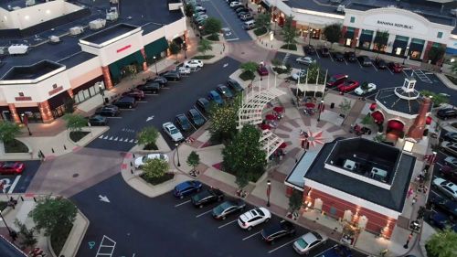 Aerial view of a shopping center with parked cars, trees, and a central plaza featuring a decorative design.