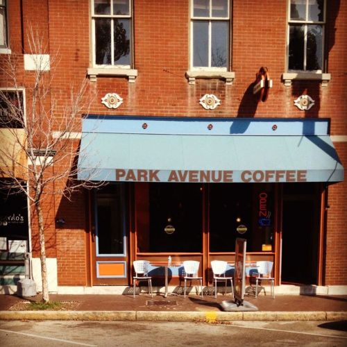 Exterior of Park Avenue Coffee with a blue awning, open sign, and outdoor seating on a sunny day.