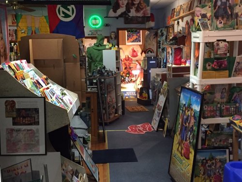 A colorful, cluttered store interior filled with artwork, posters, and various collectibles, with boxes in the background.