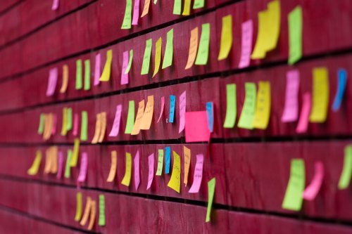 A wall covered with colorful sticky notes in various sizes and colors, arranged in a grid pattern.