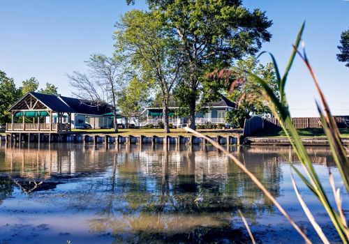 A serene waterfront scene with a calm lake, green trees, and a cozy building reflected in the water.