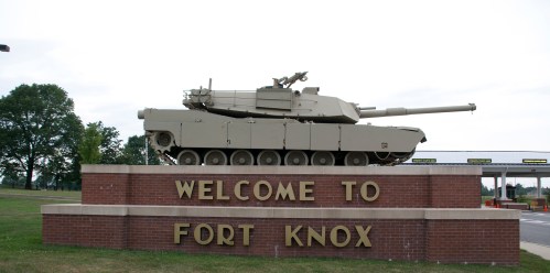 A tank displayed on a brick pedestal with the words "Welcome to Fort Knox" against a cloudy sky.