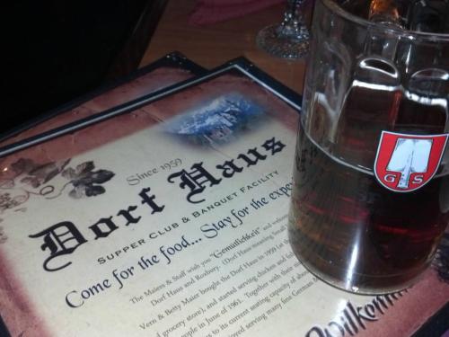 A menu from Dorf Haus Supper Club with a glass of beer beside it, showcasing a cozy dining atmosphere.