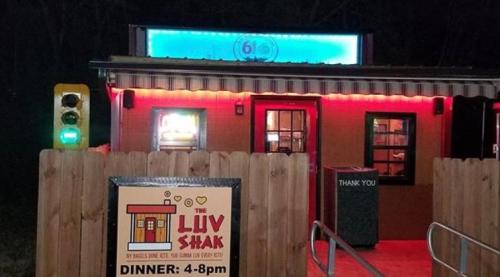 A brightly lit restaurant called "The Luv Shak" with a sign indicating dinner hours, surrounded by a wooden fence.