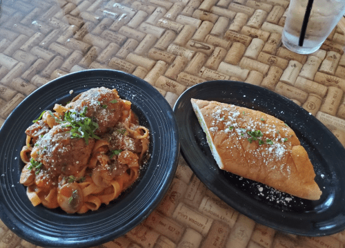 A plate of fettuccine with meatballs and marinara sauce, alongside a golden calzone, both garnished with herbs.