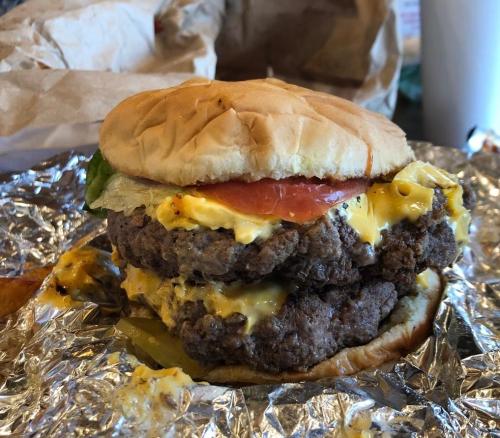 A double cheeseburger with melted cheese, lettuce, and tomato, served on a bun and wrapped in foil.