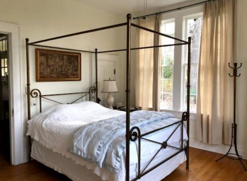 A cozy bedroom featuring a four-poster bed, light curtains, and a decorative painting on the wall.