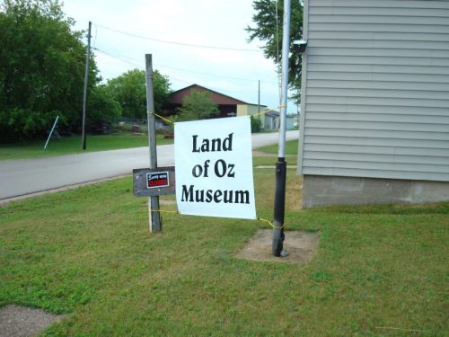 Sign for the Land of Oz Museum, displayed on a post near a road, with a "Sorry, Closed" notice below.