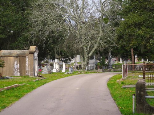 A winding path through a cemetery, lined with gravestones and surrounded by trees.
