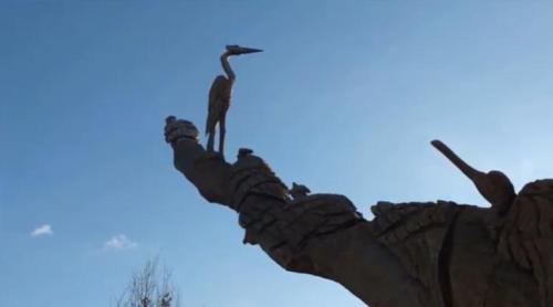 A sculpture of a heron perched on a branch against a clear blue sky.