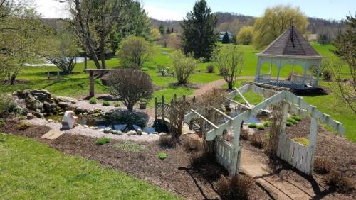 A serene garden scene featuring a pond, gazebo, and a person sitting by a small pond surrounded by greenery.
