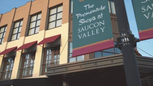 Sign for "The Promenade Shops at Saucon Valley" on a building with windows and awnings.