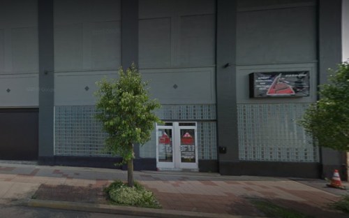 Exterior view of a building with a glass block wall, a small tree, and a sign above the entrance.