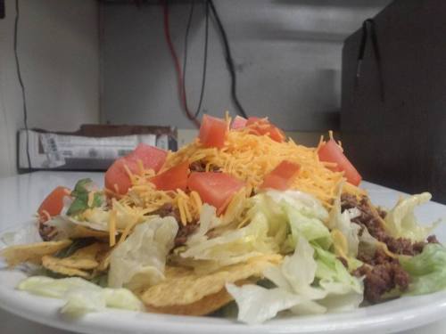 A plate of nachos topped with lettuce, diced tomatoes, and shredded cheese, served in a casual dining setting.