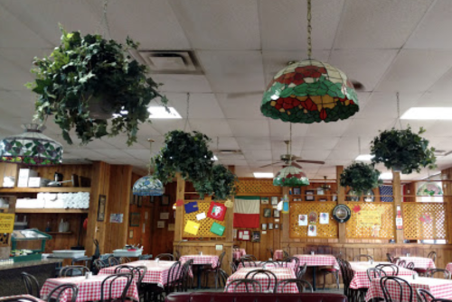 Cozy restaurant interior with checkered tablecloths, hanging stained glass lamps, and greenery. Colorful decor on walls.