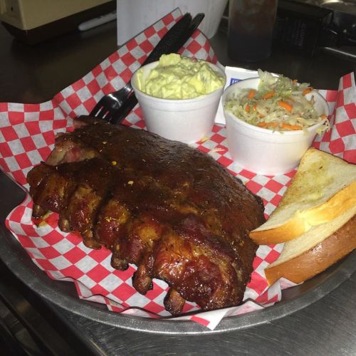 A plate of barbecue ribs with sides of coleslaw, potato salad, and two slices of bread, served in a basket.