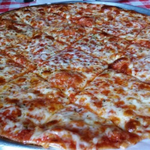 A close-up of a large, cheesy pizza with a golden crust, cut into square slices on a silver tray.