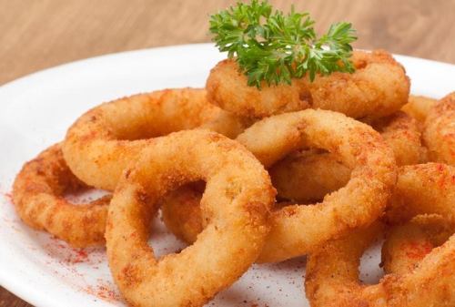 A plate of crispy, golden-brown onion rings garnished with a sprig of parsley.