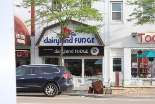 Sign for "Dairyland Fudge" in Wisconsin, with a storefront and parked car in front.