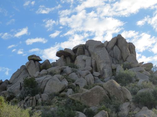 Rocky outcrop against a blue sky with scattered clouds, surrounded by sparse vegetation.