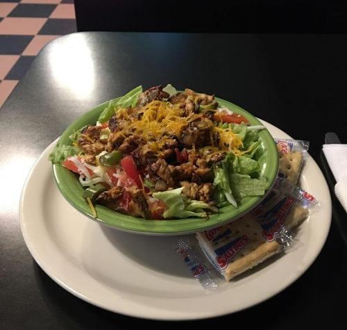 A colorful salad bowl with grilled chicken, lettuce, tomatoes, cheese, and crackers on a plate.