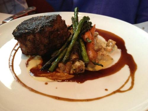 A plated dish featuring a seared beef filet, asparagus, carrots, and a rich sauce on a white plate.