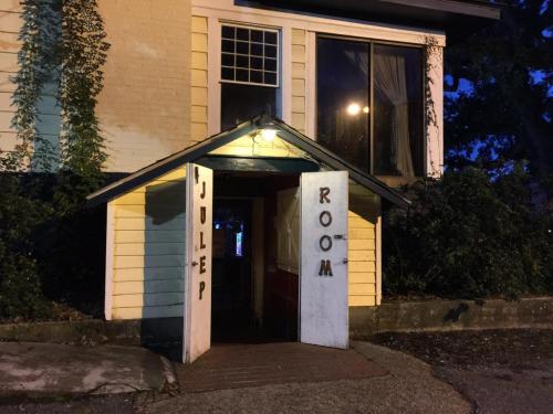 A quaint building with a sign reading "Julep Room" above an open door, surrounded by greenery at dusk.
