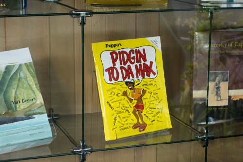 A colorful book titled "Pidgin to Da Max" displayed on a glass shelf among other books.
