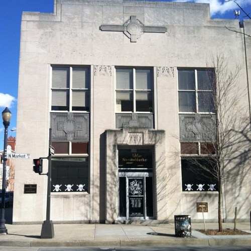 Art Deco-style building with decorative elements, large windows, and a prominent entrance. Street corner view.