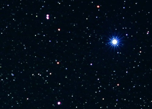 A starry night sky filled with numerous stars, featuring a bright blue star radiating light in the center.