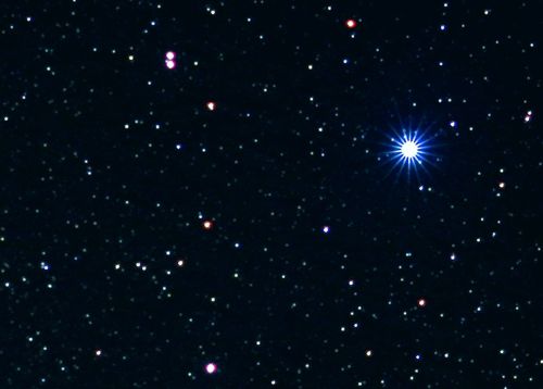A night sky filled with stars, featuring a bright blue star radiating light among smaller, colorful stars.