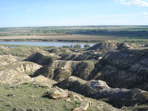 A panoramic view of rolling hills and a river, with lush green fields in the background under a clear blue sky.