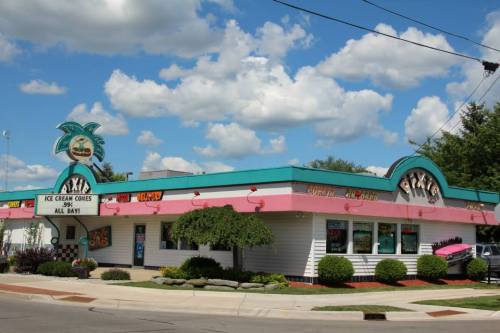 Colorful ice cream shop with a palm tree sign, pink accents, and a bright blue sky with fluffy clouds.