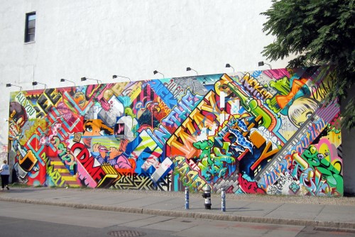 Colorful graffiti mural on a wall featuring vibrant designs, characters, and abstract patterns in an urban setting.