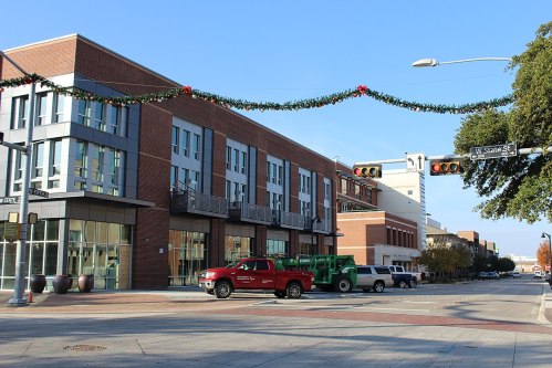 A city street scene featuring decorated buildings, traffic lights, and parked vehicles under a clear blue sky.