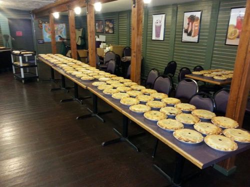 A long table filled with numerous baked pies in a cozy indoor setting.