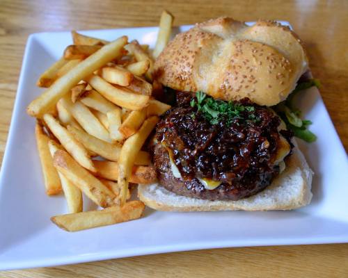 A plate featuring a juicy burger with melted cheese, topped with caramelized onions, and a side of golden French fries.