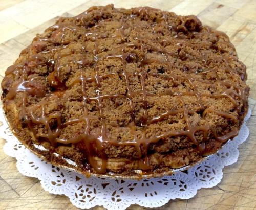 A freshly baked pie with a crumbly topping and caramel drizzle, resting on a decorative white doily.