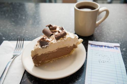 A slice of chocolate cream pie topped with whipped cream and chocolate shavings, next to a cup of coffee and a guest check.