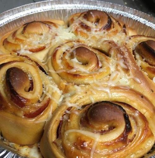 A close-up of freshly baked cheese and pepperoni rolls in a silver baking dish, golden brown and spiraled.