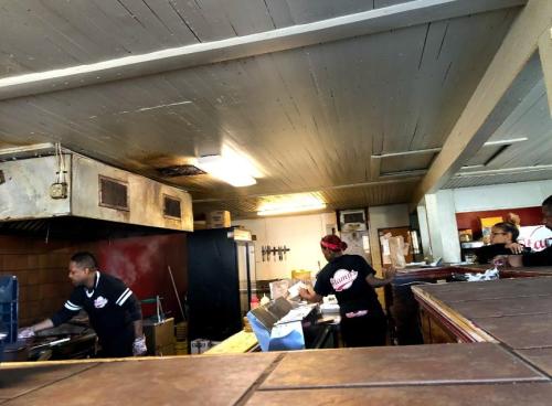 A busy kitchen with staff preparing food, featuring a grill and various cooking equipment.