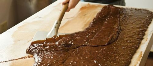A person spreads melted chocolate on a flat surface using a metal spatula.