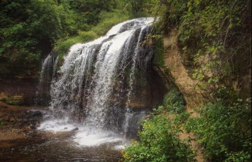 A serene waterfall cascading over rocky cliffs, surrounded by lush greenery and a tranquil stream below.