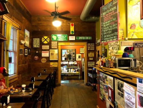 Cozy café interior with wooden walls, tables, and various signs, featuring a counter and a view into the kitchen area.